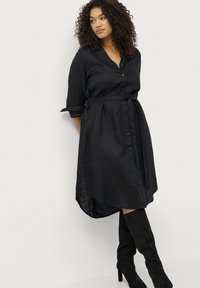 Schwarzes Leinenhemdkleid mit Knopfleiste, tailliertem Gürtel und hochgerollten Ärmeln. Verfügt über einen asymmetrischen Saum und strukturierten Stoff.