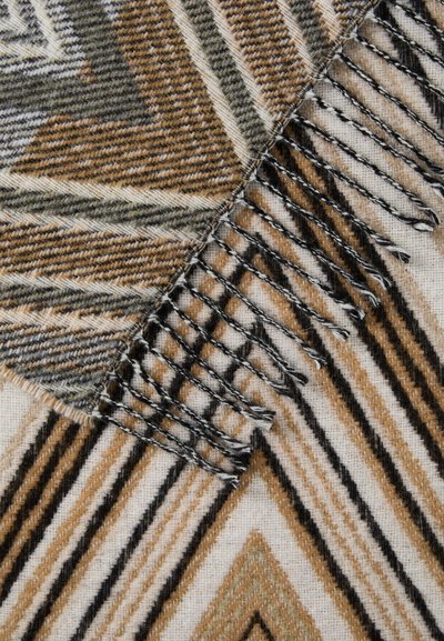 Ruskea ja kerma värinen kudottu viltti, jossa on siksak- ja raidallisia kuvioita. Varustettu helmivärein ja pehmeällä, teksturoituneella pinnalla.