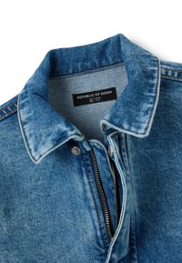 Chaqueta de mezclilla en azul claro con cuello clásico, cierre de cremallera y costuras contrastantes. La etiqueta dice "REPÚBLICA DEL MEZCLILLA."