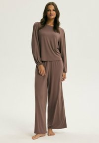 Brązowy zestaw odzieży codziennej składający się z długiego rękawa z marszczonymi rękawami oraz luźnych spodni, wykonany z miękkiej, gładkiej tkaniny.