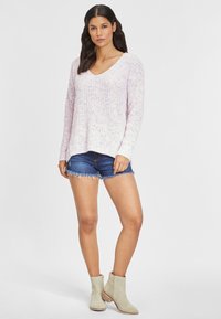 Helles rosa und weiße gestrickte Pulli mit V-Ausschnitt, kombiniert mit blauen Jeansshorts und beigen Ankle Boots. Der Pulli hat eine lockere Passform und ein geripptes Muster.