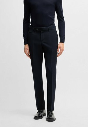 Pantaloni da abito navy su misura realizzati in tessuto testurizzato, con frontale piatto, passanti per cinture e vestibilità slim, abbinati a scarpe nere.