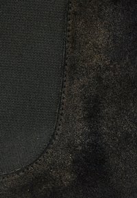 Gros plan sur un cuir suédé noir avec un panneau en tissu élastique cousu, montrant un contraste de texture entre le suède lisse et le tissu côtelé.