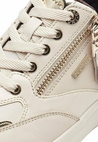 Valge nahast toss, millel on külgvärk, tekstuuritud detailid, kuldne riistvarajõud ja paksud paelad. Tootja DUO-TEX bränd on nähtav.