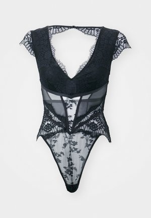 Musta bodysuit, jossa on pitsiakoristeita, läpikuultavia paneeleja, syvä V-aukko ja lyhyet hihat. Kankaan pintana on kukkakuosi, joka tuo tekstuuria ja yksityiskohtia.