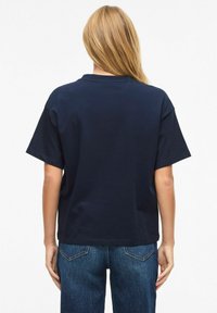 Námořnicky modré bavlněné tričko s volným střihem, krátkými rukávy a kulatým výstřihem. Pohled zezadu ukazuje jednoduchý design bez viditelných log.