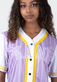 Maglietta da baseball viola e bianca con righe verticali, dettagli gialli, bottoni e "KANI" ricamato in lettere bianche sul davanti.