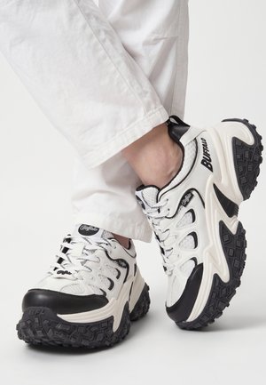 Hvide og sorte Buffalo chunky sneakers båret med hvide bukser, der viser detaljeret sål og meshstofdesign.