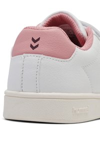 Weiße synthetische Sneaker mit strukturierter Oberfläche, rosa Ferseneinsatz und prägierter Logo. Verfügt über zwei dunkle Chevron-Akzente nahe der Oberkante.
