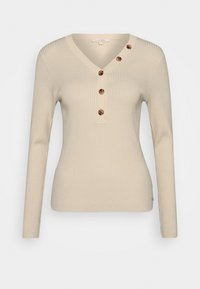 Haut beige à manches longues côtelé avec un col en V et une patte de boutonnage dotée de quatre boutons ronds marron. Tissu doux avec une coupe ajustée.