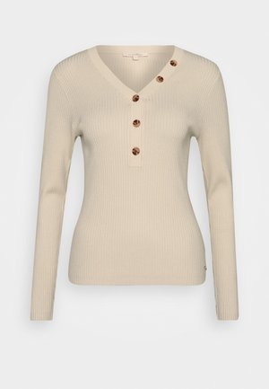 Haut beige à manches longues côtelé avec un col en V et une patte de boutonnage dotée de quatre boutons ronds marron. Tissu doux avec une coupe ajustée.