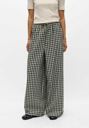 Pantalon large fluide à carreaux noir et blanc avec taille à cordon, porté avec un haut beige clair à manches courtes et des chaussures noires.
