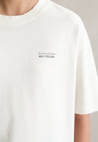 T-shirt en coton blanc avec un col rond, portant une petite impression noire qui dit "La Force de la Nature" et "MARC O' POLO DENIM".
