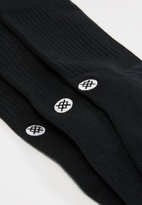 Zwarte geribde sokken met witte geborduurde logo accenten in cirkelvorm. Zachte textuur, met een aangesloten vorm ontworpen voor comfort en stijl.