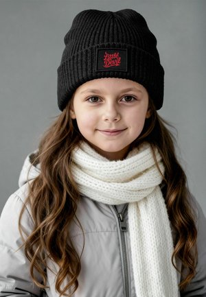 Black ribbed knit beanie with red "Little Devil" patch, cream knitted scarf. Gray zip-up jacket with a smooth finish. Brown wavy hair visible.