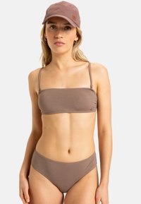 Hnedý textúrovaný bikiny top s tenkými ramienkami, spárovaný s vysokým pásom v rovnakom tóne; nosený s svetlo hnedou čiapkou so značkovou nášivkou.
