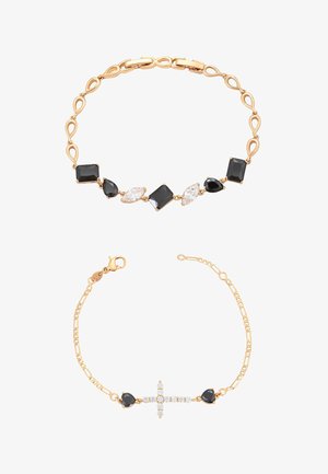Dwie złote bransoletki: jedna z czarnymi i przezroczystymi geometrycznymi kamieniami, druga z małym krzyżykiem z przezroczystych kamieni otoczonym czarnymi kamieniami w kształcie serca.