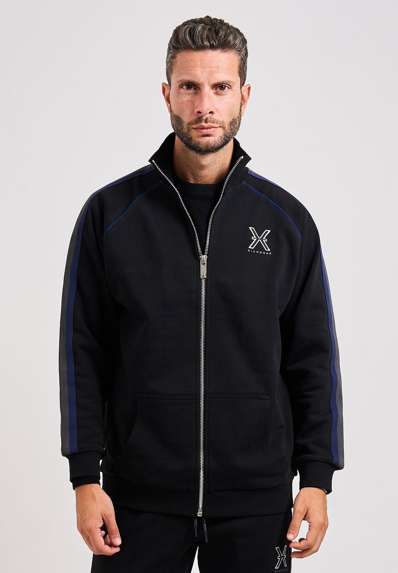 Felpa nera con zip e colletto alto, caratterizzata da strisce di accento blu sulle maniche e logo frontale. Realizzata in tessuto morbido, ha tasche frontali.