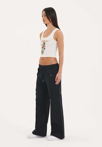 Hvid cropped tanktop med grafisk print, parret med sorte cargo bukser med lommer og snøre i taljen, båret med hvide sneakers.