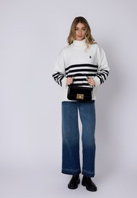 Hvid sweater med sorte vandrette striber, parret med brede blå jeans og sorte chunky støvler. Modellen holder en sort glossy håndtaske.