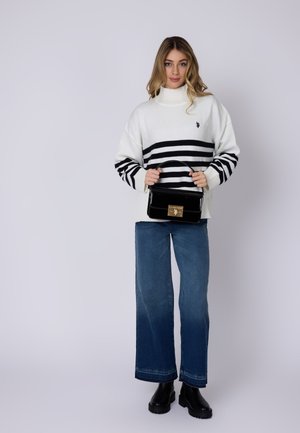 Vit tröja med svarta horisontella ränder, tillsammans med vida blå jeans och svarta klumpiga stövlar. Modellen håller en svart blank handväska.