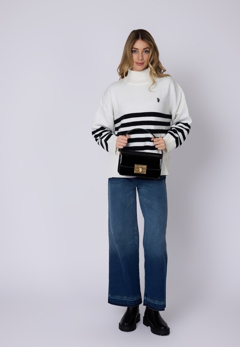 Hvid sweater med sorte vandrette striber, parret med brede blå jeans og sorte chunky støvler. Modellen holder en sort glossy håndtaske.