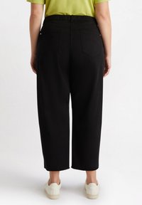 Czarne spodnie o szerokich nogawkach z elastycznym paskiem w talii, z dwoma tylnymi kieszeniami i skróconym dołem, w połączeniu z białymi trampkami.