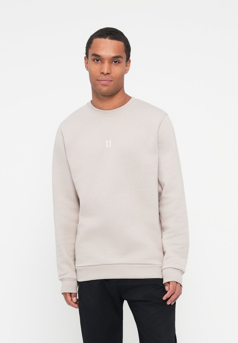 Sudadera gris claro hecha de tejido suave, con cuello redondo, puños acanalados y un pequeño logo blanco centrado en el pecho.