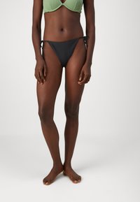Črne bikini hlačke z vezanjem na straneh, narejene iz gladkega blaga. Ponašajo se z minimalnim dizajnom in nizkim rezom, kar omogoča enostavno kombiniranje.