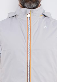 Gilet grigio chiaro con colletto alto, zip frontale con una striscia multicolore e una texture liscia e resistente all'acqua.