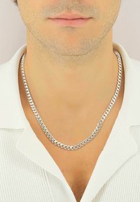 Collana in argento con anelli intrecciati. Finitura lucida e spessore medio, indossata sopra una camicia bianca con texture.
