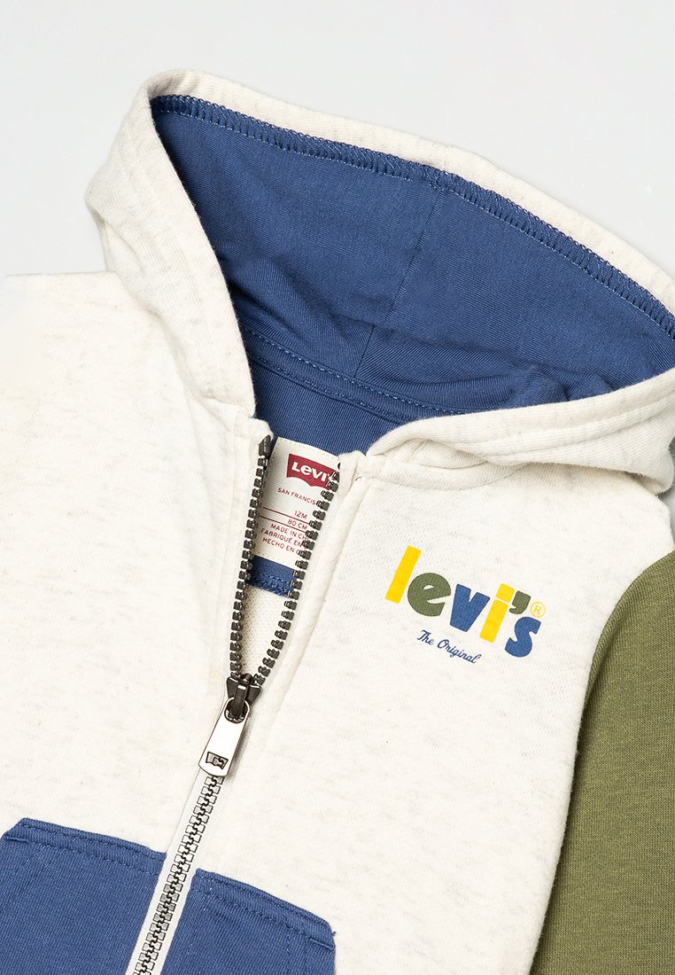Felpa Levi's con corpo crema, accenti blu e verdi, chiusura completa con zip e logo sul petto. Texture morbida con design a pannelli variabili.
