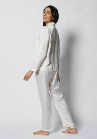 Set de pijama din satin alb, format dintr-o cămașă cu mânecă lungă și guler, alături de pantaloni largi asortați, evidențiind o textură netedă și lucioasă.