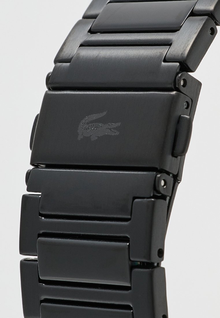 Cierre de reloj de metal negro con pulsera enlazada que presenta un logo de cocodrilo en relieve en la hebilla del cierre.