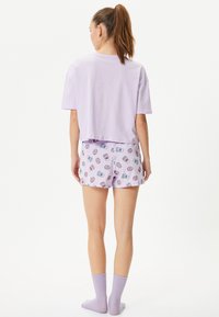 T-shirt di cotone lavanda con maniche corte abbinato a pantaloni corti con grafiche di ciambelle in rosa e blu, completato da calze viola.