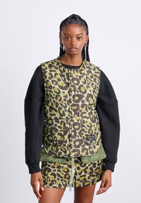 Grønn og brun leopardmønstret vest med knappelukking og to frontlommer, kombinert med et matchende mønstrete miniskjørt.