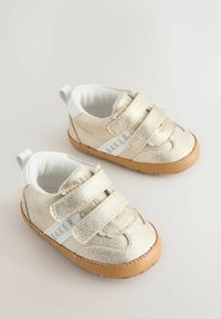 Chaussures texturées dorées avec des brides en velcro, une doublure blanche et une semelle en caoutchouc beige. Elles présentent un logo sur le côté et une boucle au talon pour un enfilage facile.