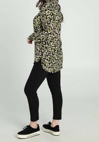 Blusa a maniche lunghe con stampa leopardata verde e crema, abbinata a pantaloni neri aderenti e sneakers nere con plateau. Tessuto texturizzato e fessure laterali.