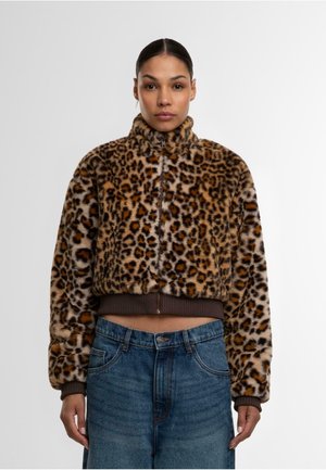 Kuttet leopardmønstret jakke med høy krage og brun ribbestrikket kant. Laget av mykt stoff, med markante svarte og oransje flekker på en beige bakgrunn.
