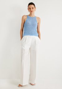 Vaaleansininen ribattu neuletoppi, joka on yhdistetty valkoisiin leveälahkeisiin housuihin. Topissa on ohuet hihnat ja hieman lyhyempi malli.