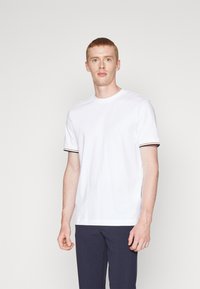Weißes kurzärmliges T-Shirt aus Baumwolle mit gerippten schwarzen und bunten Streifenakzenten an den Ärmeln, runder Ausschnitt und lockerer Schnitt.