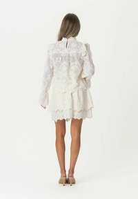 Weißes Spitzenkleid mit langen, gerafften Ärmeln und gestuftem Rock. Verfügt über komplizierte Blumenmuster und eine Schlüsselöffnung im Rücken.