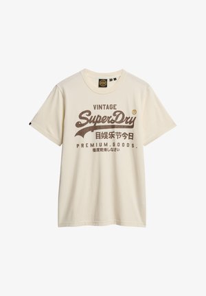 Kremowa bawełniana koszulka z krótkim rękawem, z dużym, brązowym tekstem i logo w stylu vintage z przodu. Okrągły dekolt, luźny krój.