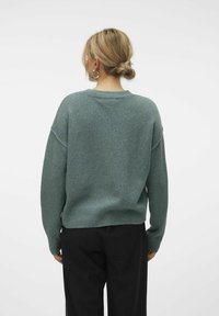 Prilagojen pulover v potopljeni teal barvi, izdelan iz mehkega pletenega materiala. Opremljen je z nizkimi rameni, okroglim ovratnikom in rebrastimi manšetami ter spodnjim robom.