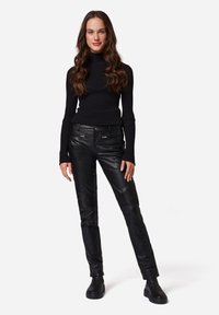 Svart ribbad turtlenecktröja kombinerad med figurnära svarta läderbyxor med dragkedjefickor och texturerade detaljer, kompletterat med stiliga svarta stövlar.