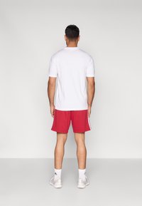 Balti trumpomis rankovėmis marškinėliai derinami su raudonais sportiniais šortais su šoninėmis juostelėmis. Dėvima su baltais sportiniais batais ir tiek aukščio kojinėmis.