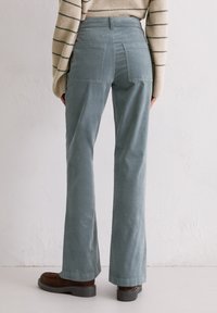 Hooggetailleerde, uitlopende broek van zachte, gedempte teal stof, met twee achterzakken en gecombineerd met donkerbruine schoenen.