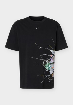 Musta Nike T-paita, jossa pieni valkoinen logo keskellä lähellä pääntietä ja värikäs halkeillut seinä kukkakuvalla alaoikealla puolella.
