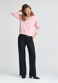 Maglione rosa chiaro con scollo a V realizzato in materiale morbido, abbinato a pantaloni neri a vita alta con gamba larga e stivaletti neri con punta.