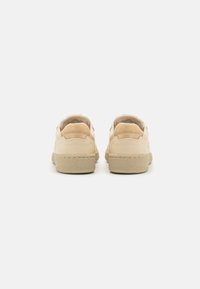 Beige lærersneakers med teksturert såle og semskede detaljer ved hælen, med avrundet design og lavt snitt.
